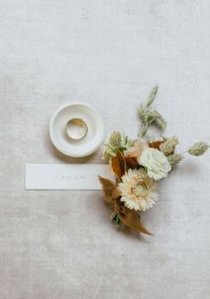 a wedding ring sits next to a bouquet of flowers on a white tablecloth with a name tag