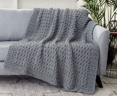 a couch with a crocheted blanket on top of it next to a potted plant