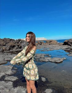 a woman standing on rocks near the ocean with her arms around her neck and looking into the distance