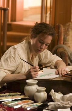 a woman sitting at a table writing on a piece of paper with a pen in her hand