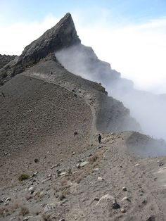 two people hiking up a mountain side with low clouds in the air and fog coming from behind them