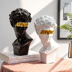 two busturines wearing blindfolds sit on top of a table next to books