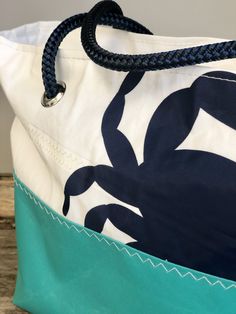 "NEW DESIGN! Handcrafted from recycled sail and aqua marine fabric, this handbag features a large blue crab cut from sail insignia. Perfectly sized for everyday use with the option of short handles or longer straps for over the shoulder comfort. Handles can be cut from natural cotton rope or navy. Bag measures approximately 16\"w x 9\"h x 5\" d and comes fully lined with a water resistant fabric. Three open interior pockets provide added organization." Everyday Sail-colored Rectangular Bag, Nautical Beach Bag In Sail Color, Sail Bags Recycled, Nautical Style Beach Tote Bag, Nautical Tote Beach Bag, Blue Nautical Beach Bag, Nautical Sail-colored Bag For Daily Use, Recycled Sails, Nautical Sail-colored Beach Bag