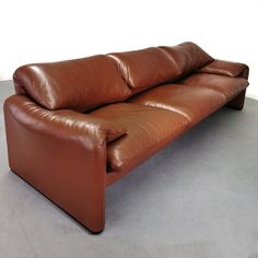 a brown leather couch sitting on top of a cement floor next to a white wall