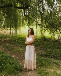 a woman standing under a tree with her arms crossed