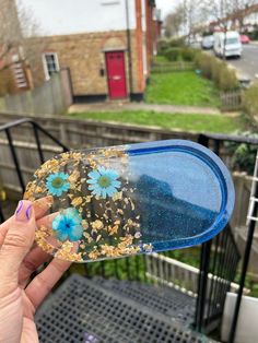 a person holding up a piece of glass with blue flowers on it and gold flakes