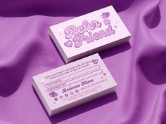 two business cards sitting next to each other on a purple cloth with hearts and stars