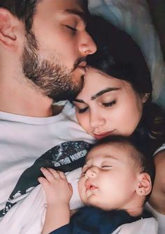 a man and woman laying next to each other holding a baby