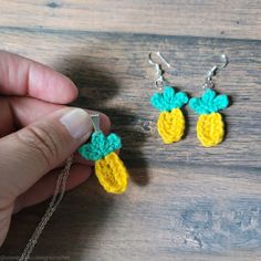 a person holding two pieces of crocheted pineapple earrings in front of a wooden table