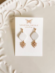 a pair of white and gold earrings sitting on top of a white plate next to a card