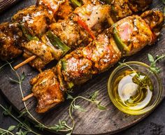 chicken skewers on a wooden platter with olive oil and herbs next to them