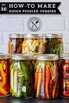 jars filled with pickled veggies sitting on top of a table next to a brick wall