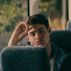 a young man sitting on a bus with his hand to his head and looking out the window