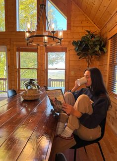 a woman sitting at a wooden table drinking from a cup and reading a book in front of her