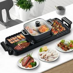 an electric grill with food on it sitting on a table next to two plates and a potted plant