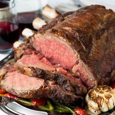 a large roast on a platter with vegetables and wine