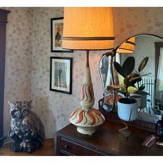 a lamp sitting on top of a wooden table next to a mirror and potted plant