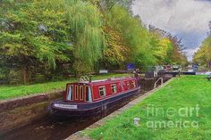 a painting of a narrow canal with boats on the side and green grass in front