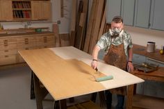 a man in an apron painting a table with a paint roller on top of it