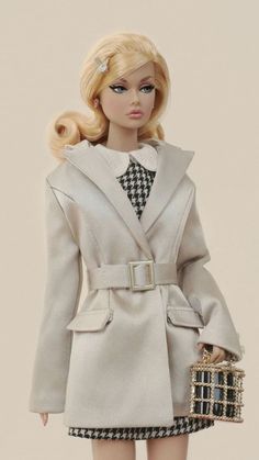 a barbie doll dressed in a coat and dress holding a purse with her hand on her hip