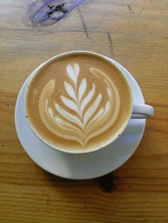 a cappuccino on a saucer sitting on top of a wooden table