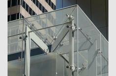 the corner of a glass building with metal brackets on it's sides and an office building in the background