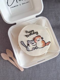 a cake in a box with a cat on it and a spoon next to it