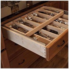 an open drawer in the middle of a kitchen with knives and spoons inside it