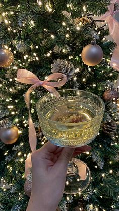 a hand holding a wine glass in front of a christmas tree