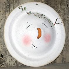 a white plate with a face painted on the front and side, hanging from a wooden wall