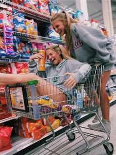 two women in grey sweatshirts pushing a shopping cart through a grocery store filled with food