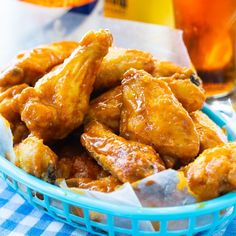 a blue basket filled with fried chicken wings next to a glass of beer and orange juice