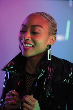 a woman with silver hair and piercings smiles at the camera while wearing a black leather jacket