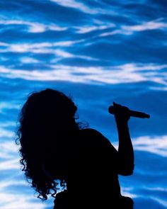 the silhouette of a woman holding a microphone in front of a large screen with blue water behind her