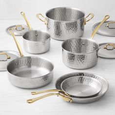 an assortment of stainless steel pots and pans with gold handles on a marble countertop