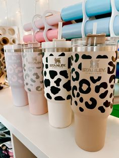 several different colored tumblers are lined up on a shelf in front of other cups