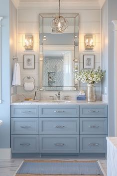 a bathroom with blue cabinets and white walls, lights above the sink and rug on the floor