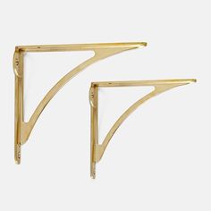 two gold metal shelf brackets against a white background, one is shaped like a triangle and the other has a curved edge