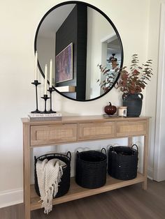 a wooden table topped with baskets under a round mirror next to a wall mounted candle holder