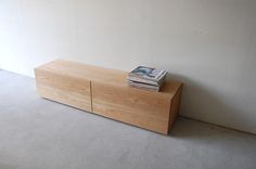 a book is sitting on top of a wooden cabinet in an empty room with white walls