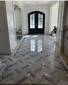 an empty room with marble flooring and black door in the center, surrounded by white walls