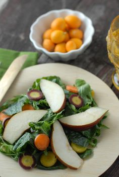 a salad with apples, carrots and radishes on a plate next to a glass of orange juice