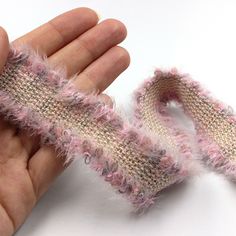 a hand holding a piece of fabric with pink and white yarn on it, in the palm of someone's left hand