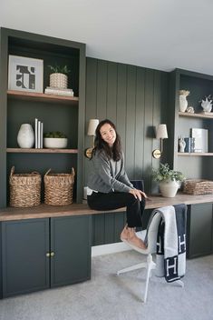 a woman sitting on top of a desk next to a shelf filled with books and baskets