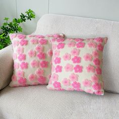 two pink and white pillows sitting on top of a couch next to a potted plant