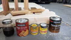 four cans of paint sitting on top of a wooden table next to a piece of wood