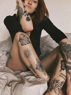 a woman sitting on top of a bed with tattoos on her arms and legs