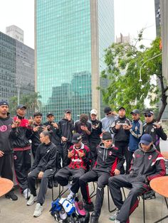 a group of young men sitting next to each other on chairs in front of tall buildings