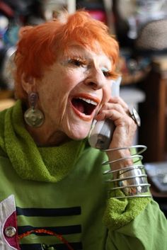 an older woman with red hair is talking on the phone and laughing at someone else