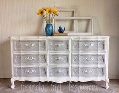 a white dresser with yellow flowers on top and blue vases sitting on top of it